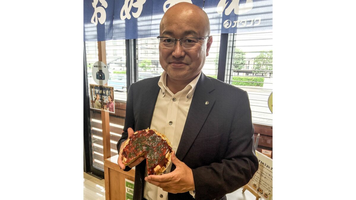 Otafuku Sauce Co. President Naoyoshi Sasaki, holding a plastic model of okonomiyaki used in shop windows.
