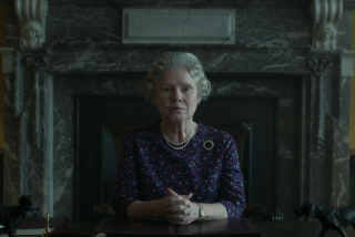 A woman sits at a desk in front of a marble fireplace.