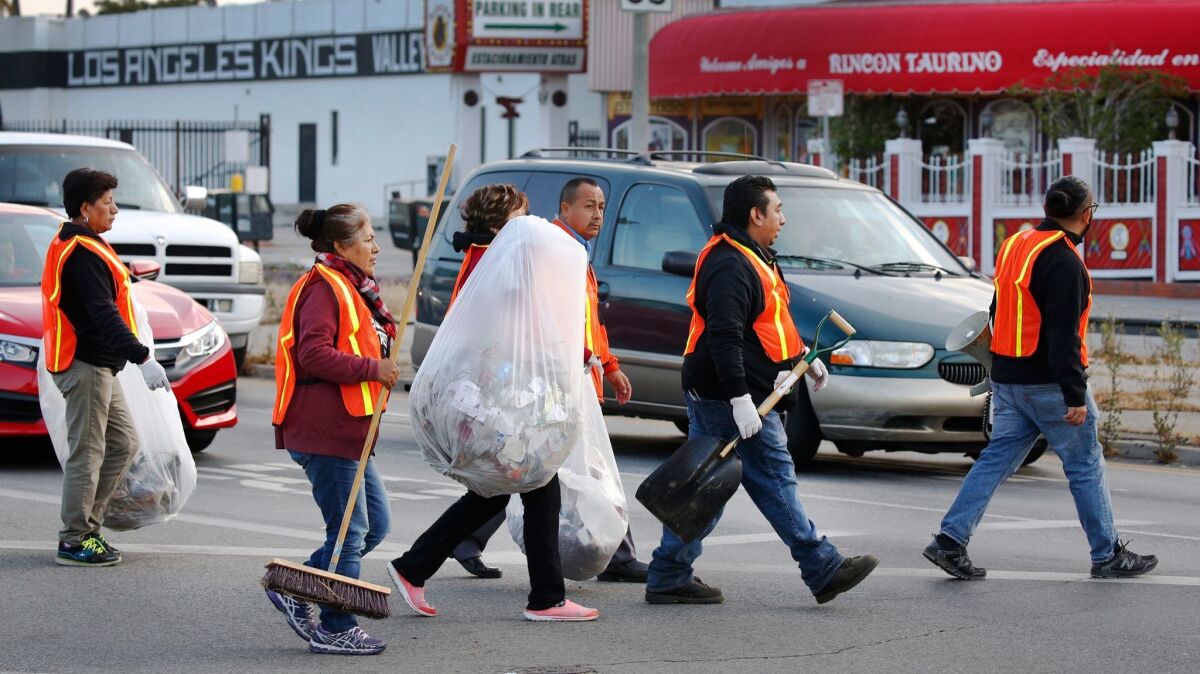 Street vendors and supporters armed with brooms and trash bags clean the street median at the intersection of Tobias Avenue and Parthenia Street in Panorama City.
