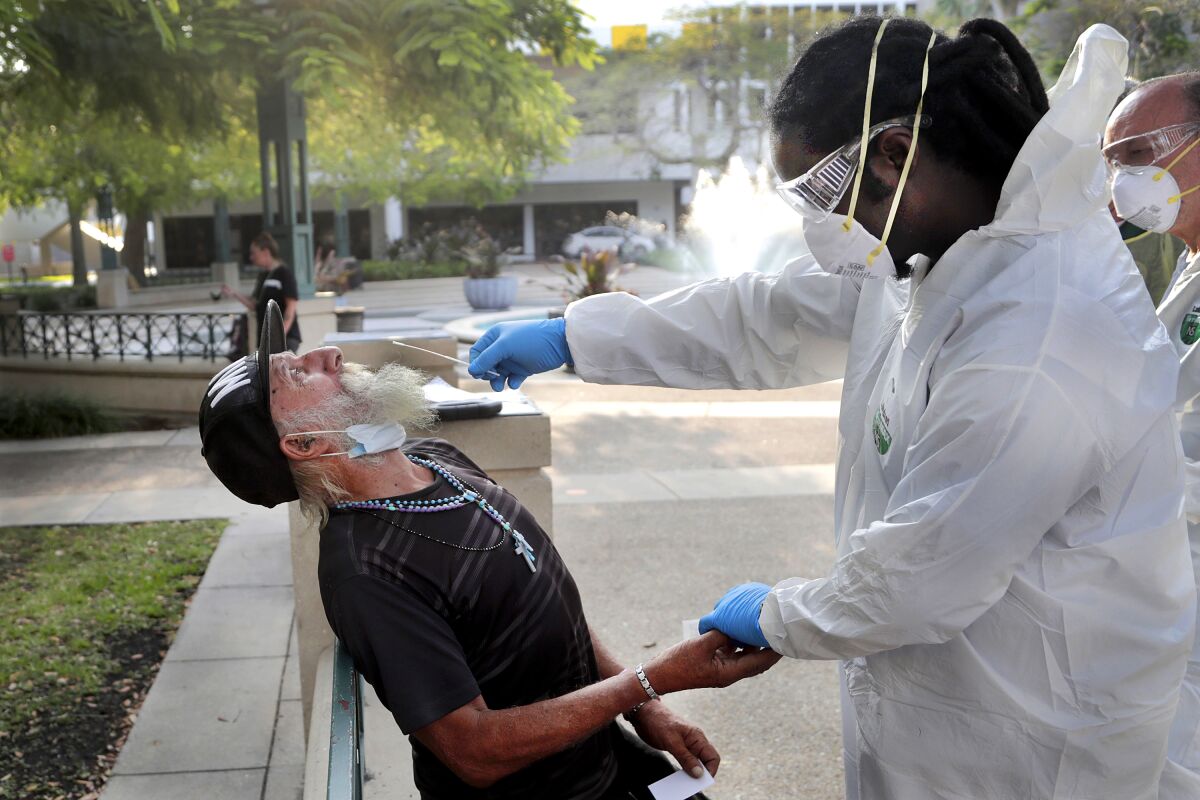 Nurse practitioner Gregory Pierre holds the hand of Leonardo Toledo Martinez while taking a swab for coronavirus testing in Miami last month.