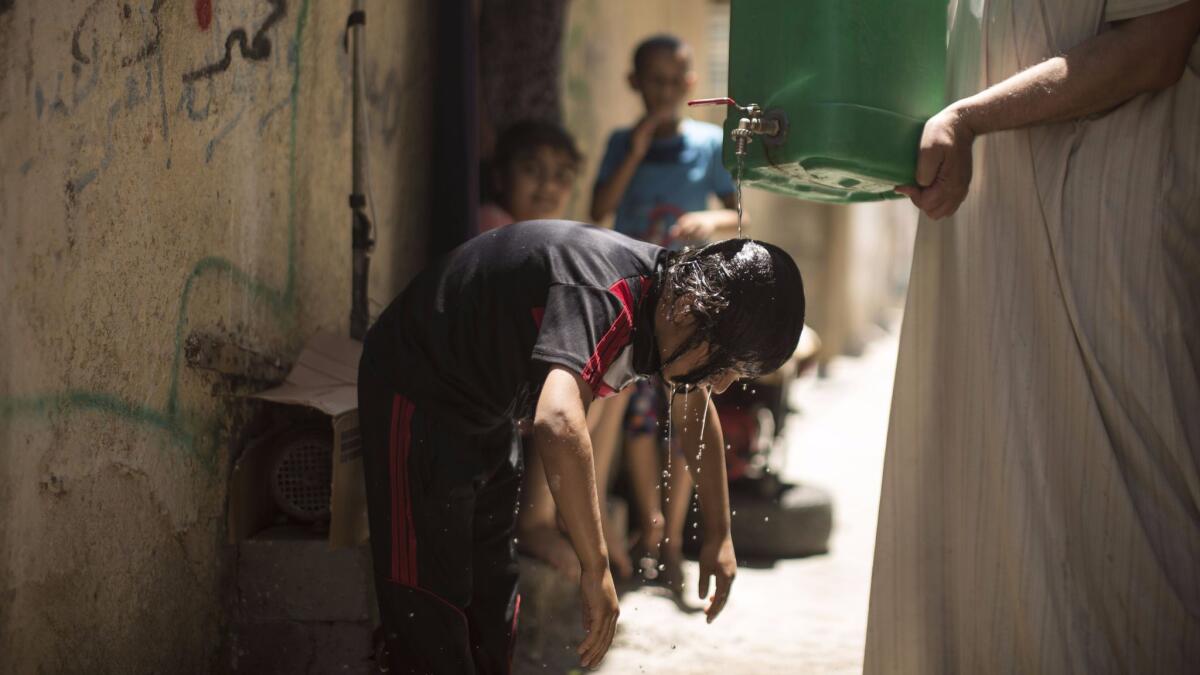 A Palestinian boy cools off with water from a jerrycan held by a man during a heatwave at al-Shati refugee camp in Gaza City on July 2, 2017.