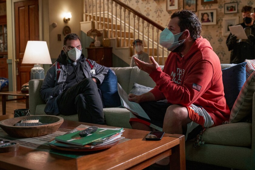 Two men wearing masks sit on a couch