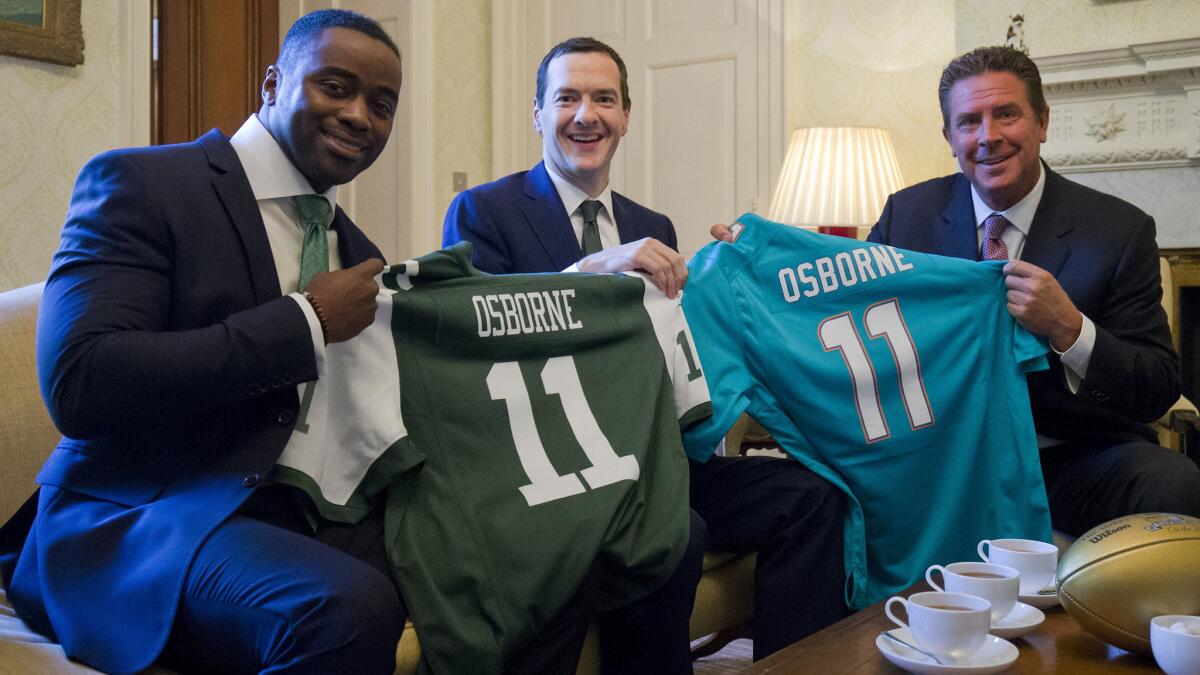 Former NFL stars Curtis Martin, left, and Dan Marino, right, present Britain Chancellor George Osborne with Jets and Dolphins jerseys on Friday.