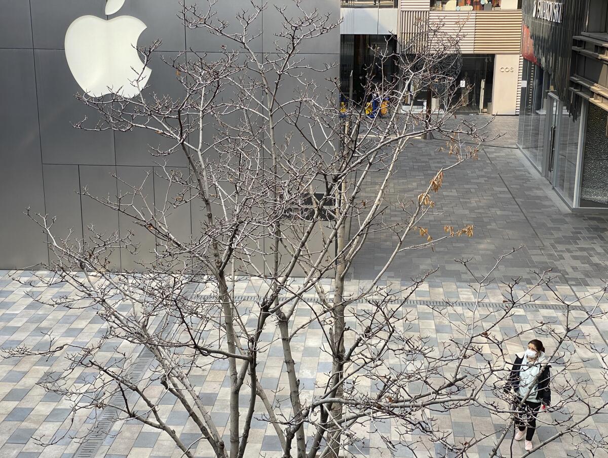 A woman in a mask walks in an empty Beijing mall district past an Apple store.
