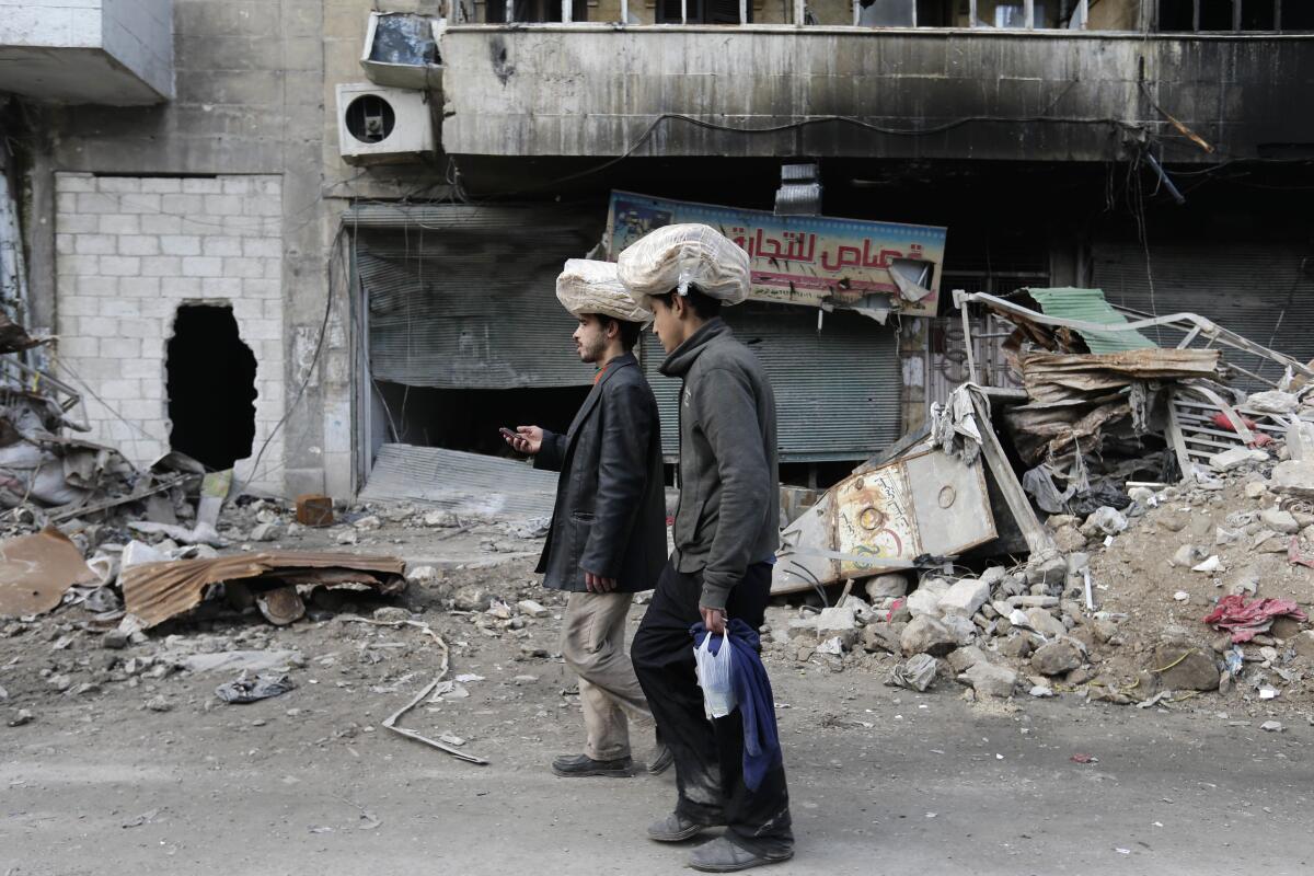 FILE - In this Jan. 20, 2017 file photo, Syrian men carry bags of bread on their heads while walking back to their homes in the once rebel-held Bustan al-Qasr neighborhood in the eastern Aleppo, Syria. As Syria marks the 10th anniversary Monday, March 15, 2021, of the start of its uprising-turned-civil war, President Bashar Assad may still be in power, propped up by Russia and Iran. But millions of people are being pushed deeper into poverty, and a majority of households can hardly scrape together enough to secure their next meal. (AP Photo/Hassan Ammar, File)