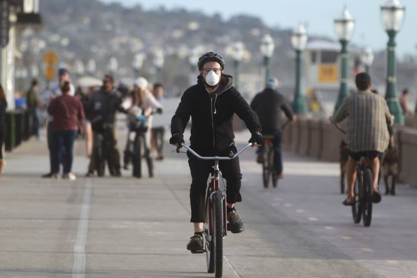 A 35-year-old Mission Hills resident, who said his name was Michael, no last name given, wears a mask as a precaution for the coronavirus as he rides his bike on the Mission Beach Boardwalk on Friday, March 20, 2020 in San Diego, California.
