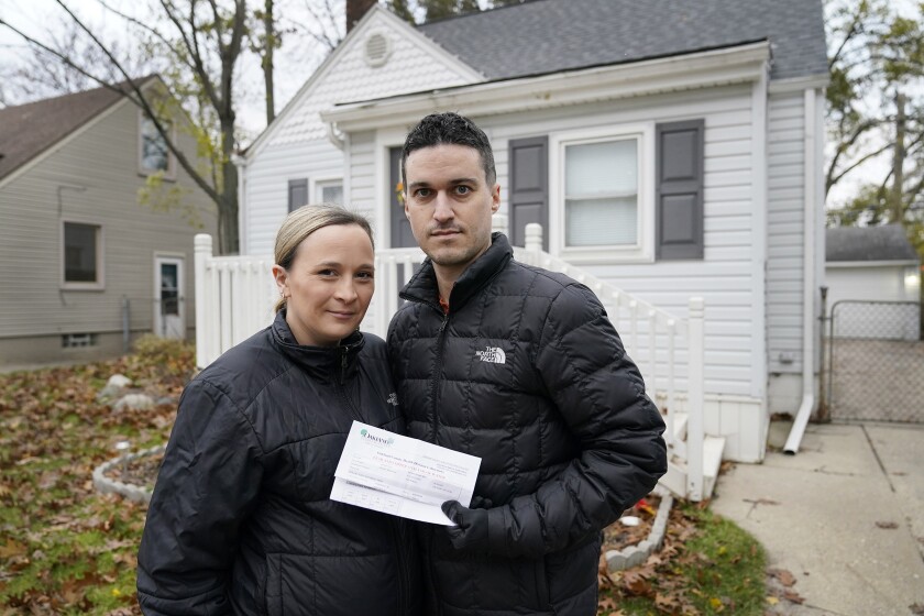 Nicole and Simon Obarto, holding a lead and copper analysis of water from the Oakland County Health Division, stand outside their home in Royal Oak, Mich., on Thursday, Nov. 18, 2021. The couple had their water line tested for lead and the results were high enough to have the lead service line replaced. (AP Photo/Carlos Osorio)