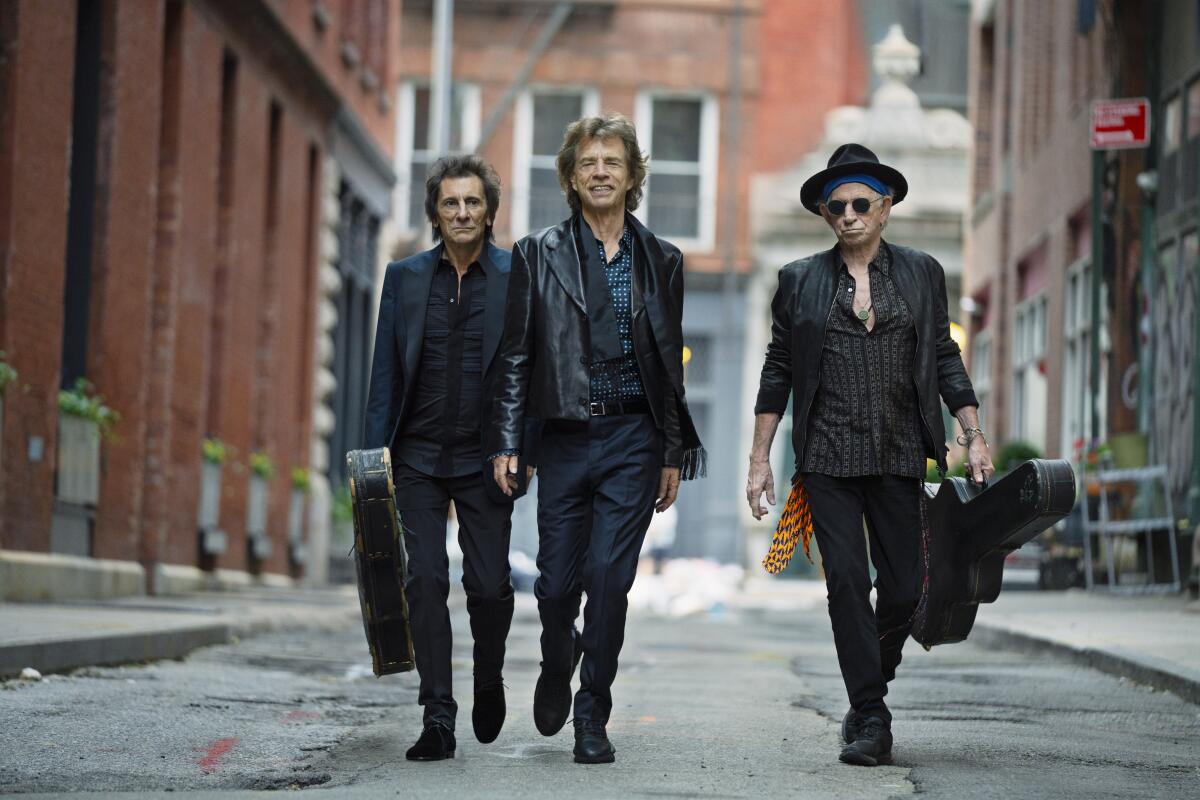 Three musicians in black walking down a city street