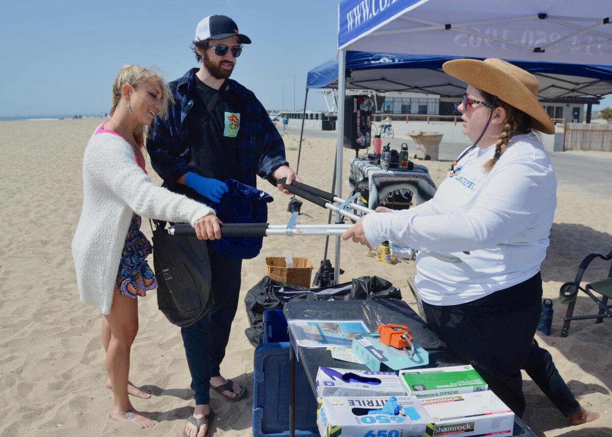 O.C. Coastkeeper volunteer coordinator Suzanne Welsh hands out beach-cleanup tongs to disc jockey DD Garth and Jace Sandell.