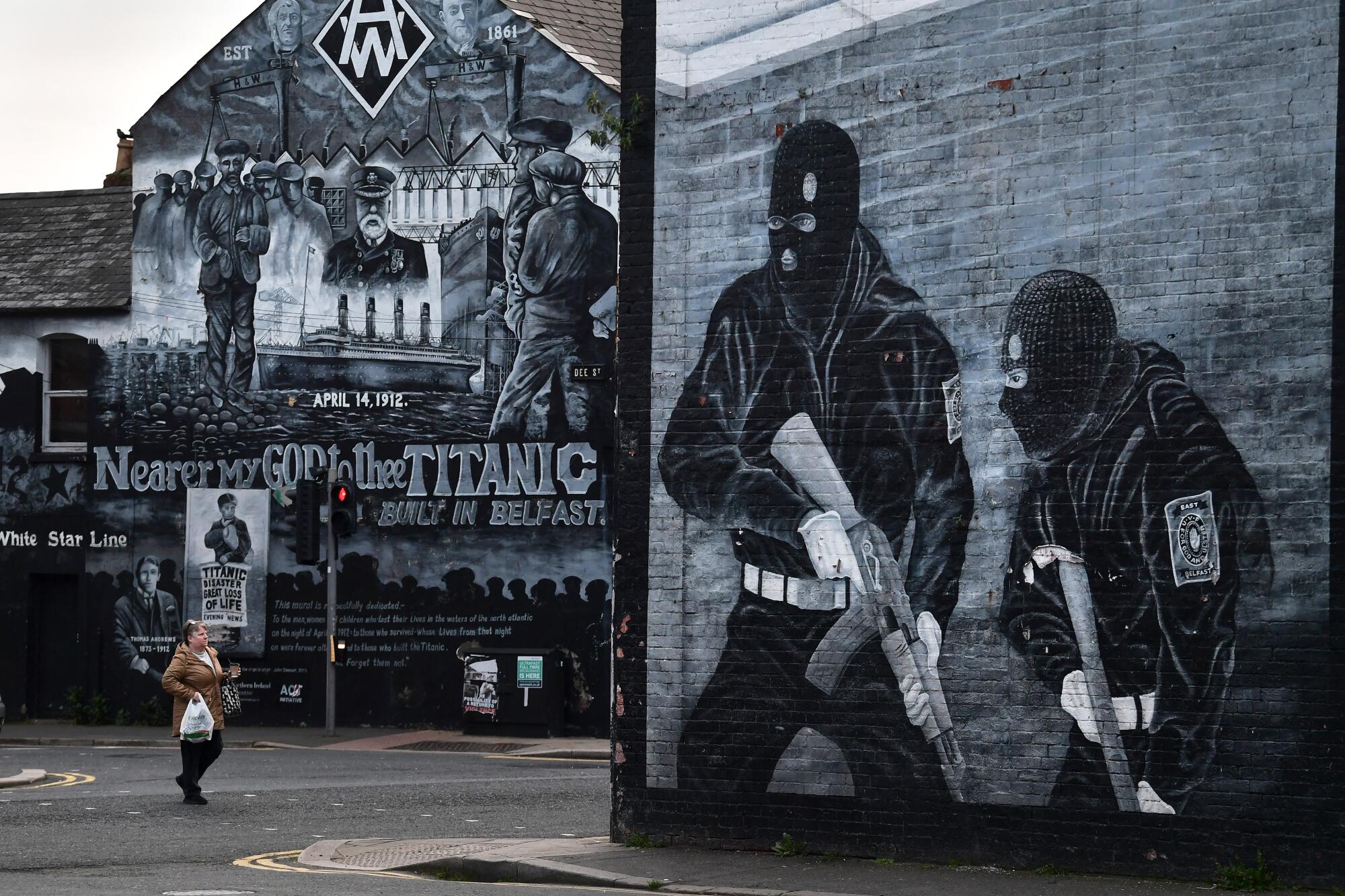 A person walks past a loyalist paramilitary mural in Belfast, which depicts two people with guns wearing balaclavas. 