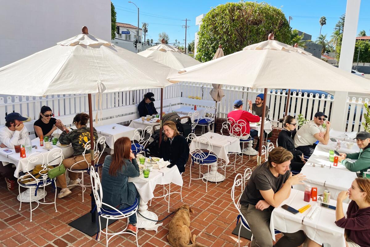 A brick patio full of guests at tables shaded by white umbrellas at Larchmont's Cookbook Cafe.
