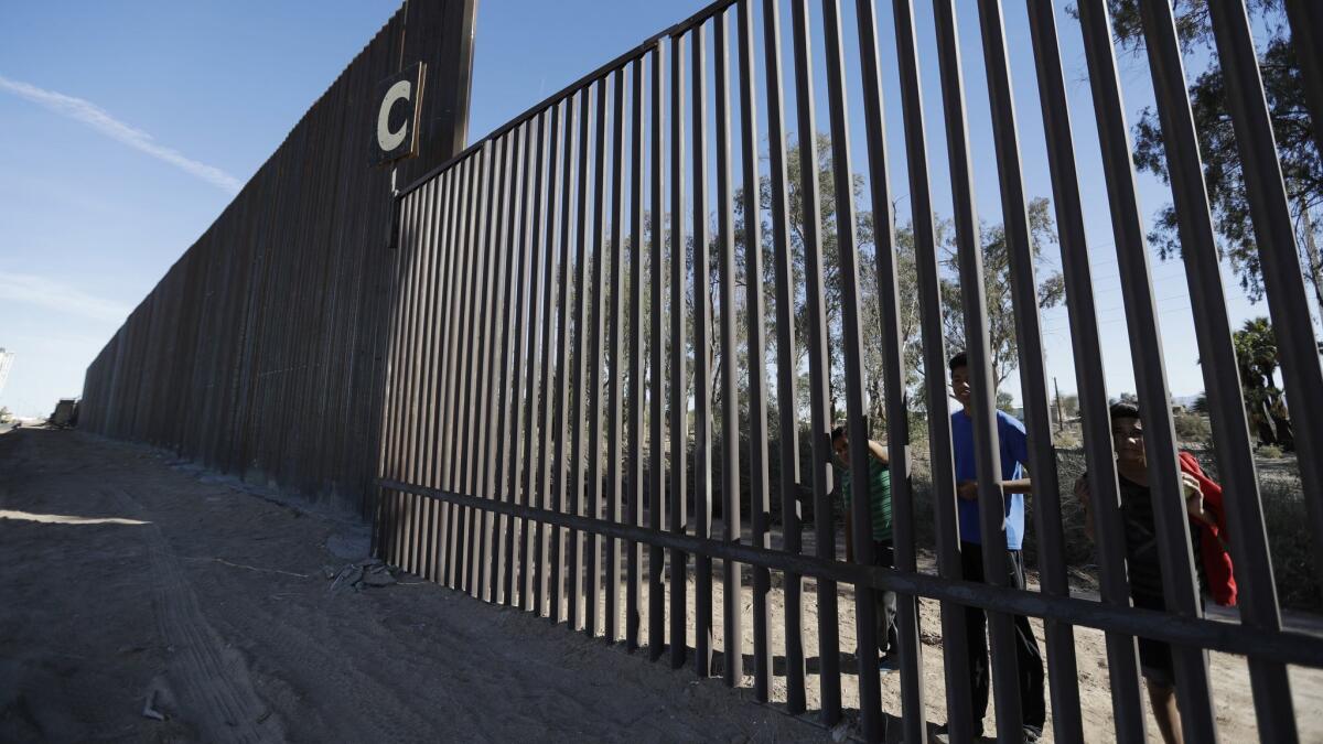Boys look through an older section of the border wall from Mexicali, Mexico, alongside a newly constructed, taller section in Calexico.