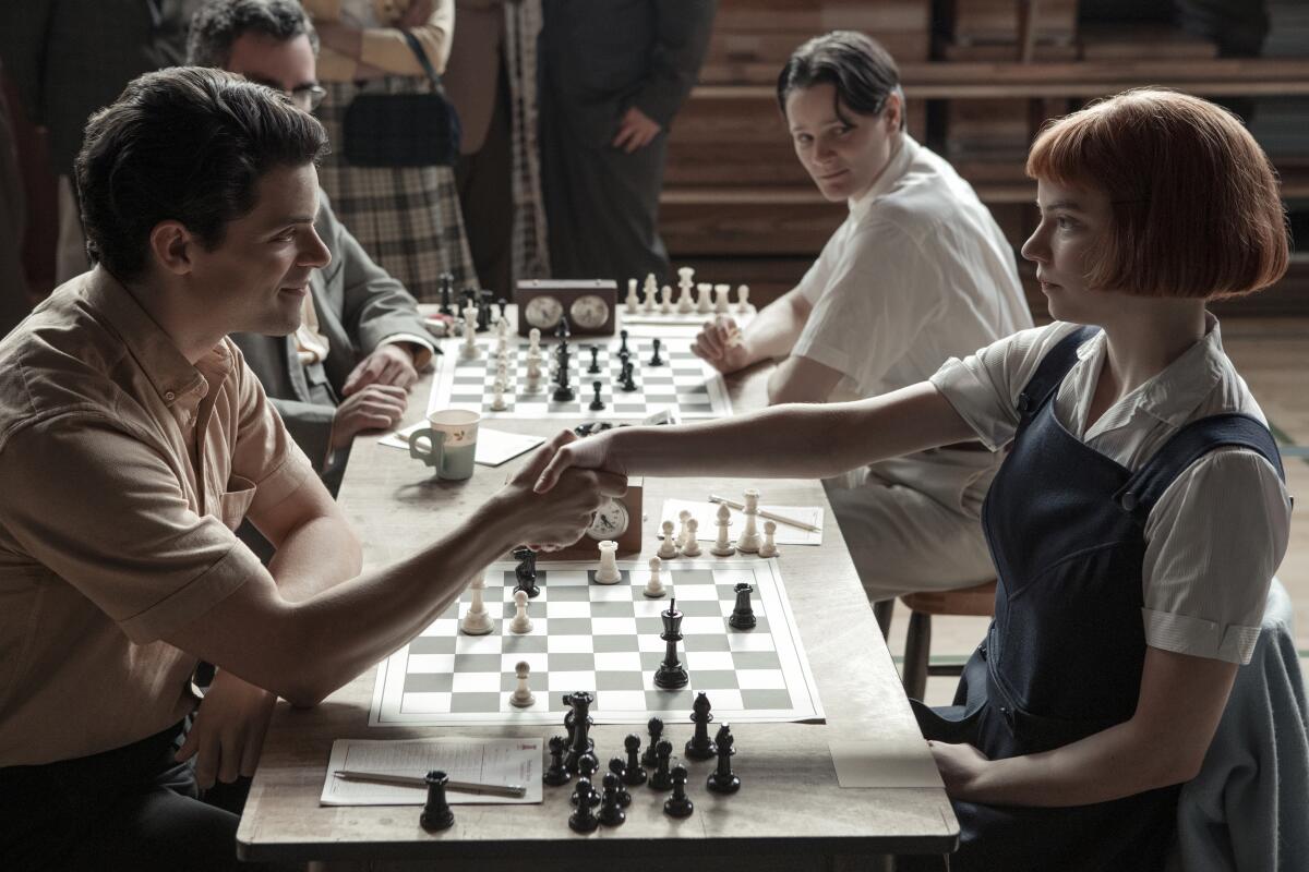 A young man and a young woman shake hands over a chess board.