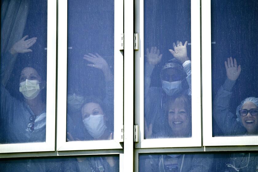 ORANGE, CA -- TUESDAY, APRIL 14, 2020: UC Irvine Medical Center health care workers bang on the windows in a return of gratitude as they watch about 25 Orange County first responders vehicles participate in a drive-by parade of gratitude as they battle COVID-19 at the hospital, which currently has 8 patients with the virus in Orange, CA, on April 14, 2020. (Allen J. Schaben / Los Angeles Times)