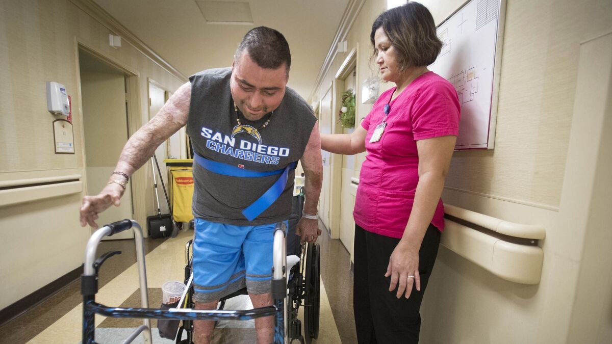 Julio Edeza, left, is assisted by Mila Fernandez, restorative nursing assistant at the Amaya Health Care Center in Spring Valley, Calif., during a physical therapy session.