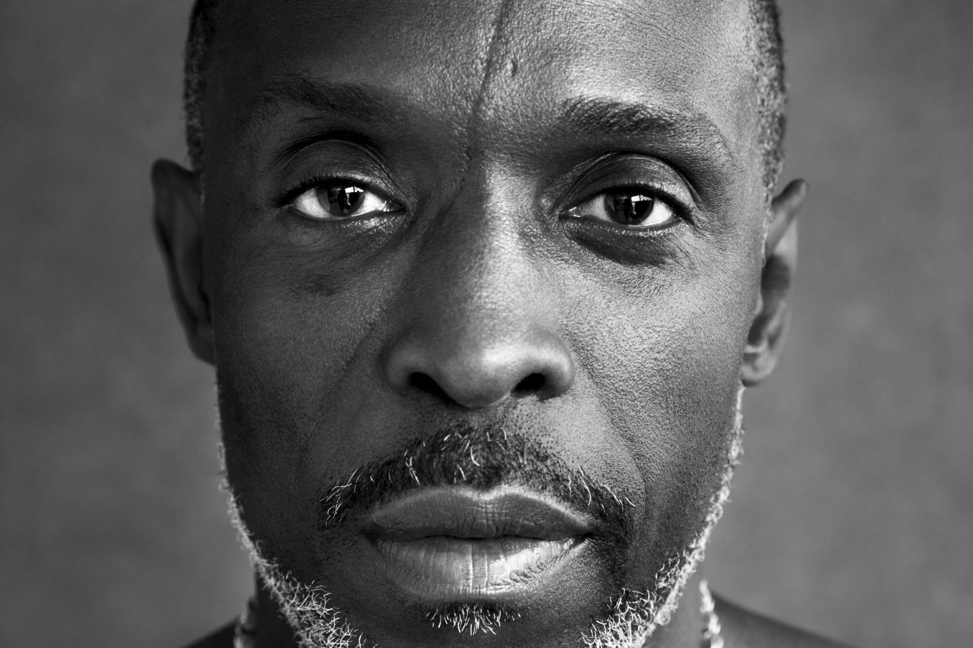 Michael K. Williams, sporting necklaces, stares at the camera