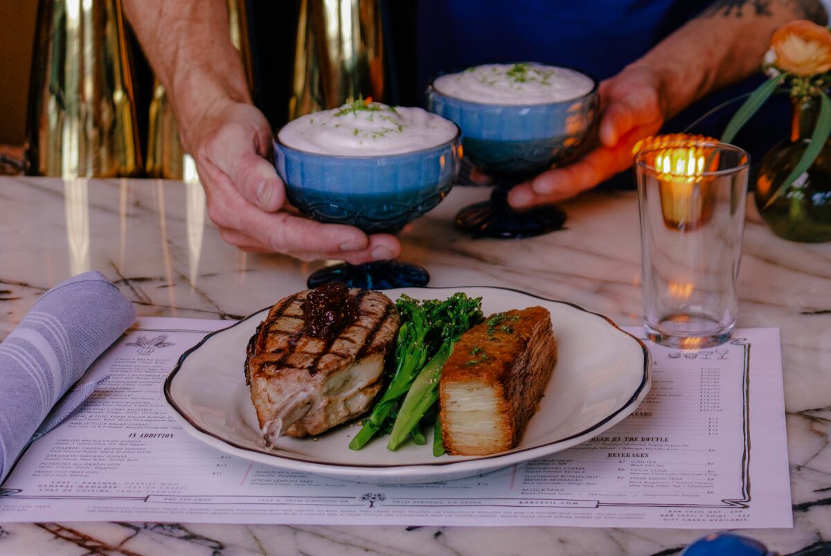 Hands hold two small dishes of sauce over a plate of smoked pork chops.