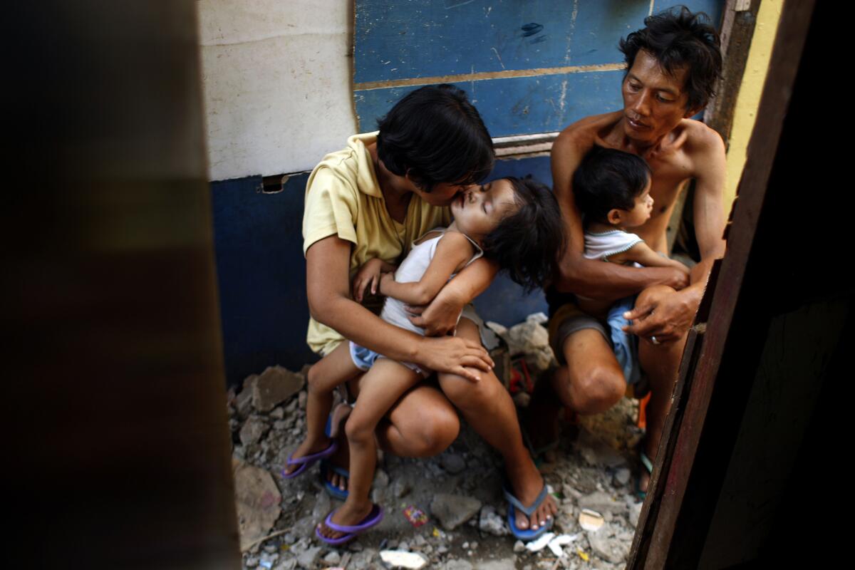 Yolanda and Noel sit in the alley outside their shack with two of their children. They scramble each day to get the money to feed the family. Although she is a Roman Catholic, Yolanda disagrees with the church's opposition to contraception and is part of a lawsuit challenging the city ban on providing birth control at public clinics.
