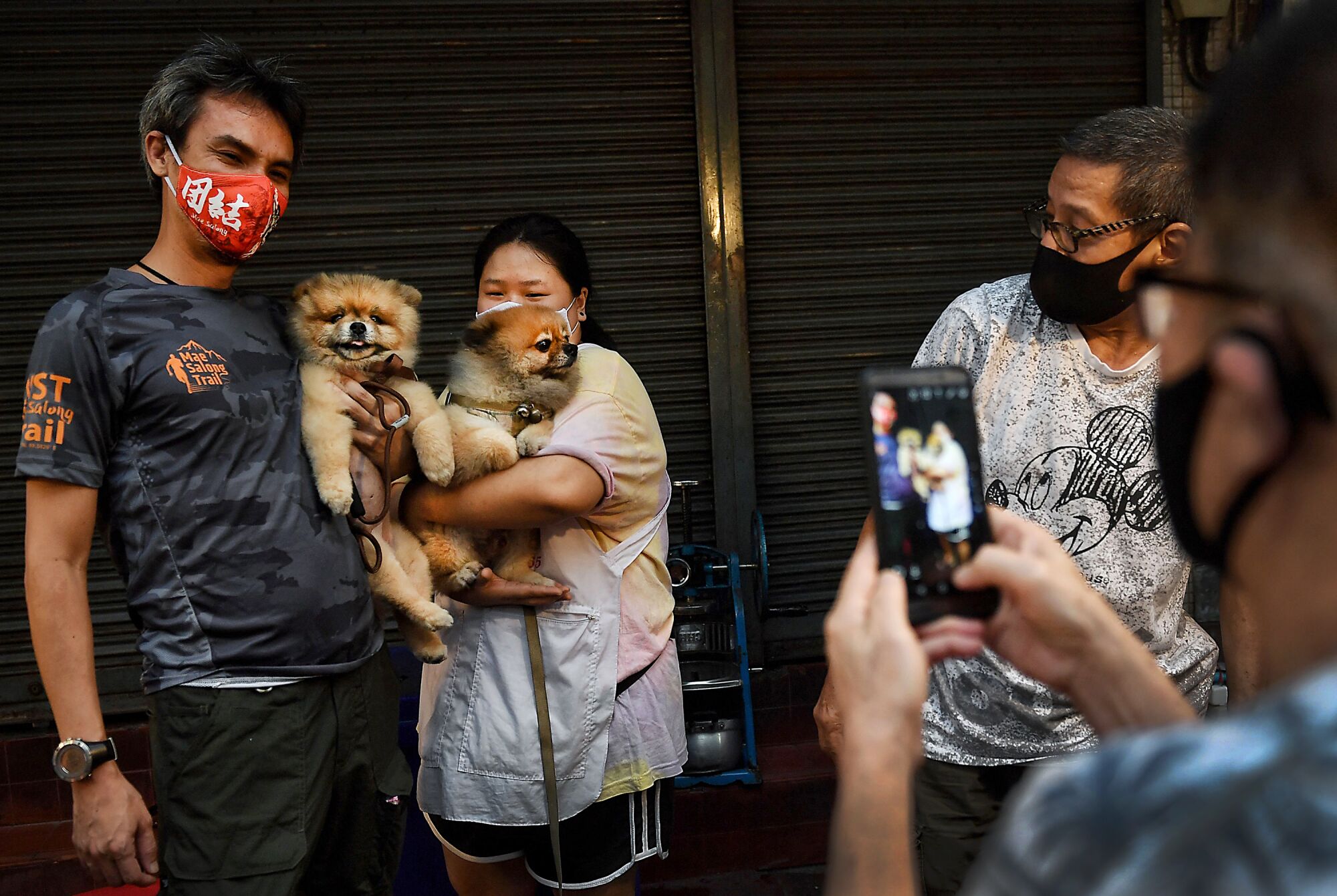 THAILAND: A street food vendor (C) and a customer (L) in face masks, as a preventive measure against the spread of the COVID-19 coronavirus, have their photo taken with their dogs in Chinatown in Bangkok on April 17, 2020.