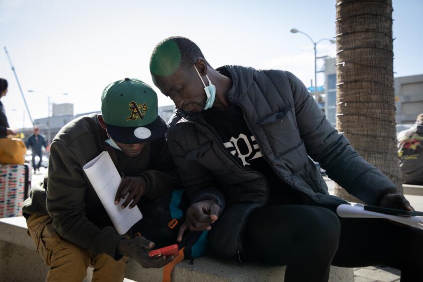 San Diego, California - February 23: Ismael Bah, center left, and Abdou Khan try to connect to the free wifi after arriving to the San Diego International Airport after being released from Border Patrol earlier in the day on Friday, Feb. 23, 2024 in San Diego, California. Khan left his country of Gambia seeking safety and plans to fly to Minnesota where he has a brother. Khan had planned to crossed into the United States through Arizona until he saw a television program about the welcome center in San Diego and decided to change his route and come to California. "I thought we would go to the center and they would help us with a bus or plane ticket," Khan said. "That's what they explained on the news." The welcome center closed Thursday. He spoke to his brother after being able to connect where his brother was able to book him a plane ticket. (Ana Ramirez / The San Diego Union-Tribune)