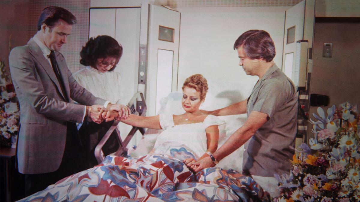 A woman sits in a hospital bed surrounded by praying people.