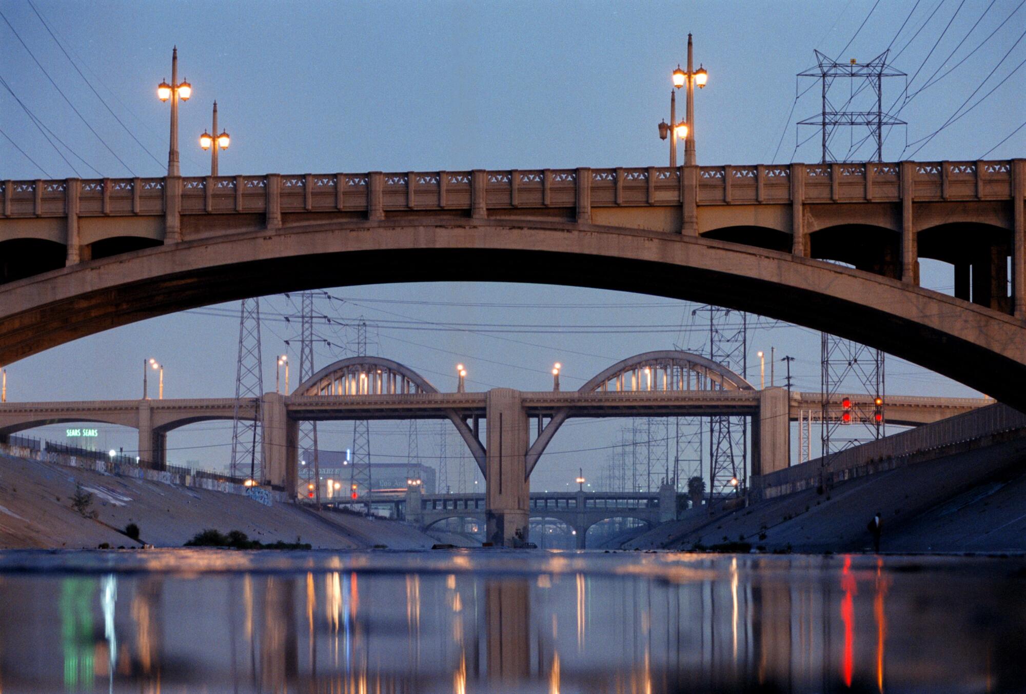 A river-level view of several bridges at twilight over the L.A. River 