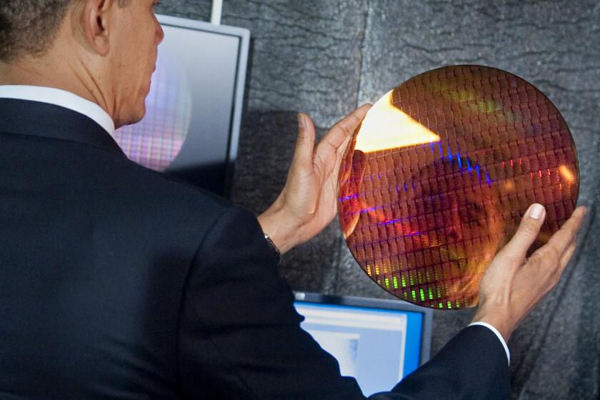 US President Barack Obama looks at his reflection as he holds an Intel wafer made of microchips