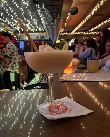 A frozen coconut margarita in a coupe glass on the bar under string lights at Casa Vega.