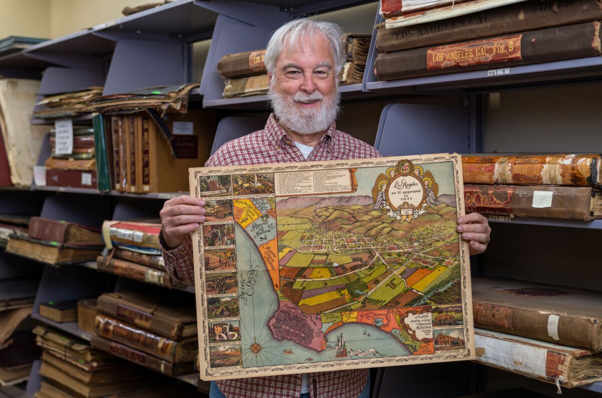 A smiling man holds up a map while standing in front of shelves of old books