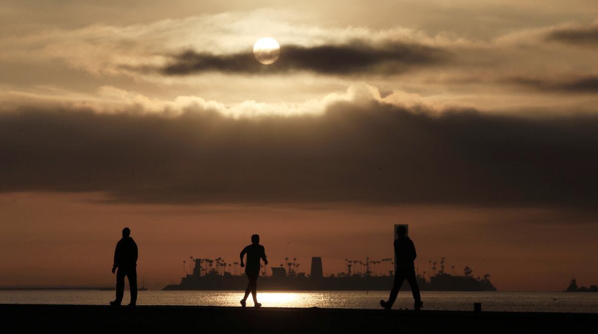 Joggers and walkers stretch their legs while the sun rises over a cloud bank along Alamitos Beach in Long Beach.