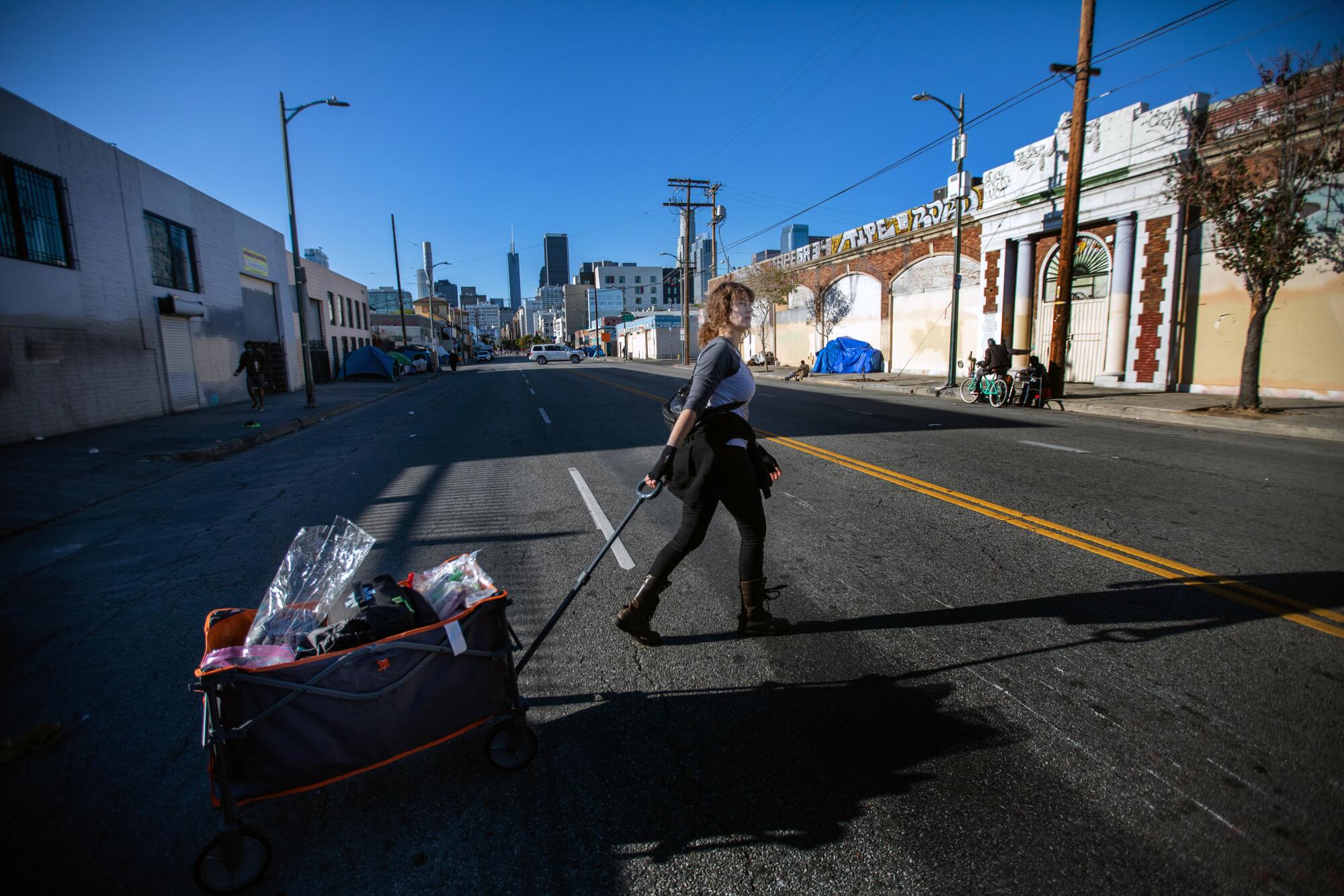 A woman pulls a cart along a street