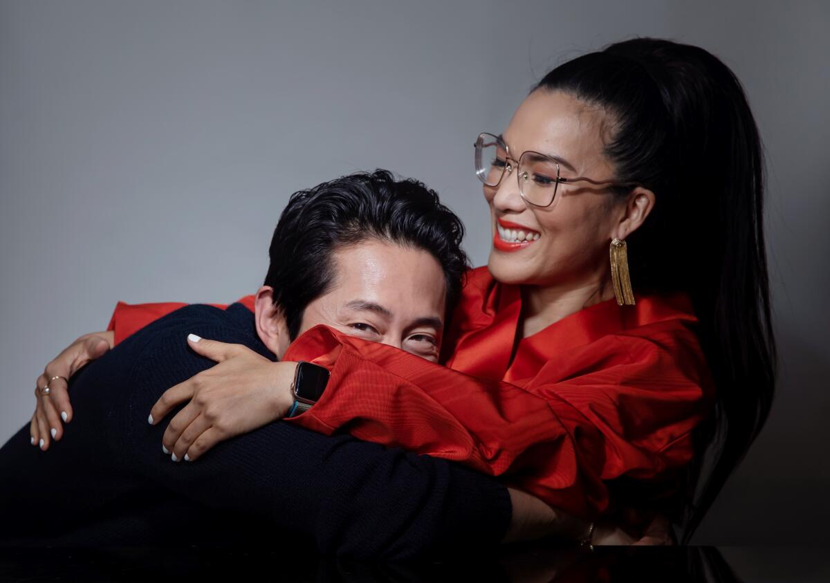 Steven Yeun, left, is hugging Ali Wong and his face is half hidden behind her arm.