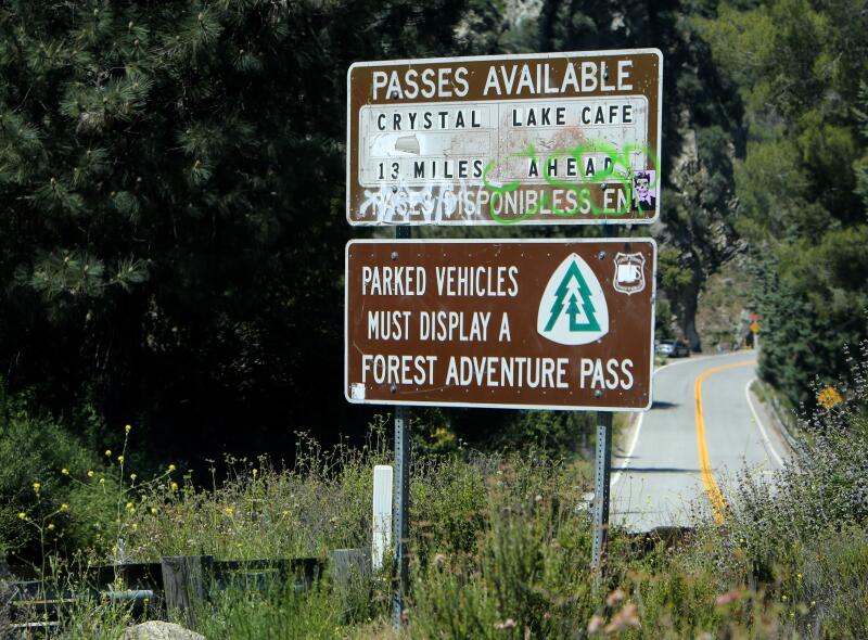 A sign that says "Parked vehicles must display a Forest Adventure Pass." along Highway 39.