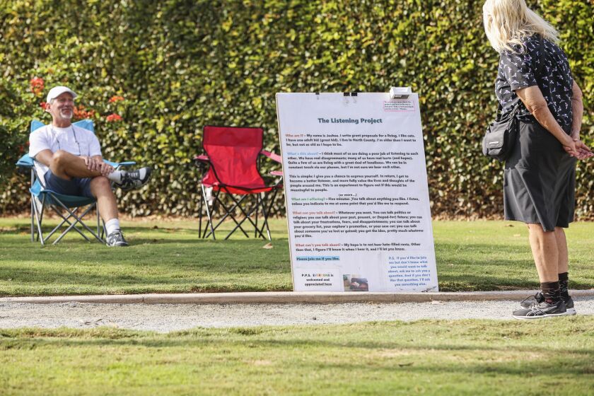 Encinitas, CA - October 12: Joshua Lazerson (left), who recently launched what he calls The Listening Project, sits in his chair as Sara Ohara reads his sign at Swami's Seaside Park on Wednesday, Oct. 12, 2022 in Encinitas, CA. Lazerson started The Listening Project as a way to invite people to sit down and talk about themselves while he listens. (Eduardo Contreras / The San Diego Union-Tribune)