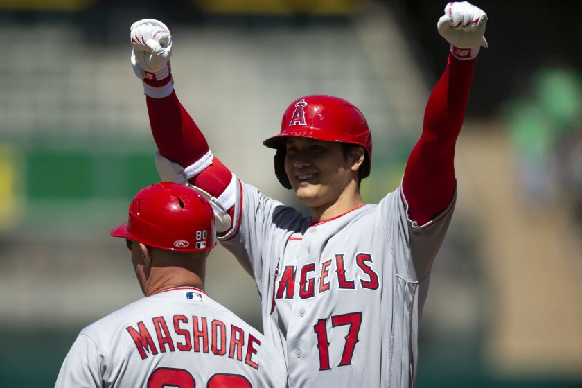 Los Angeles Angels designated hitter Shohei Ohtani (17) celebrates after hitting an RBI-single against the Oakland Athletics during the third inning of a baseball game, Saturday, April 1, 2023, in Oakland, Calif. First base coach Damon Mashore, left, looks on. (AP Photo/D. Ross Cameron)