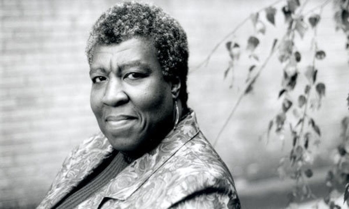 Octavia E. Butler seen sitting with leaves behind her