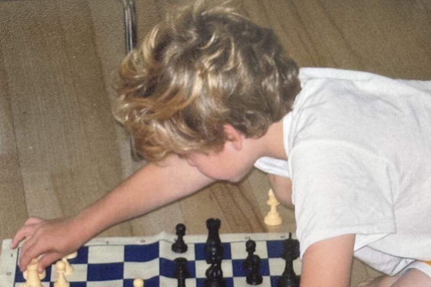 Miller Moss, shown as a child, plays chess on a cloth board placed on the floor. 