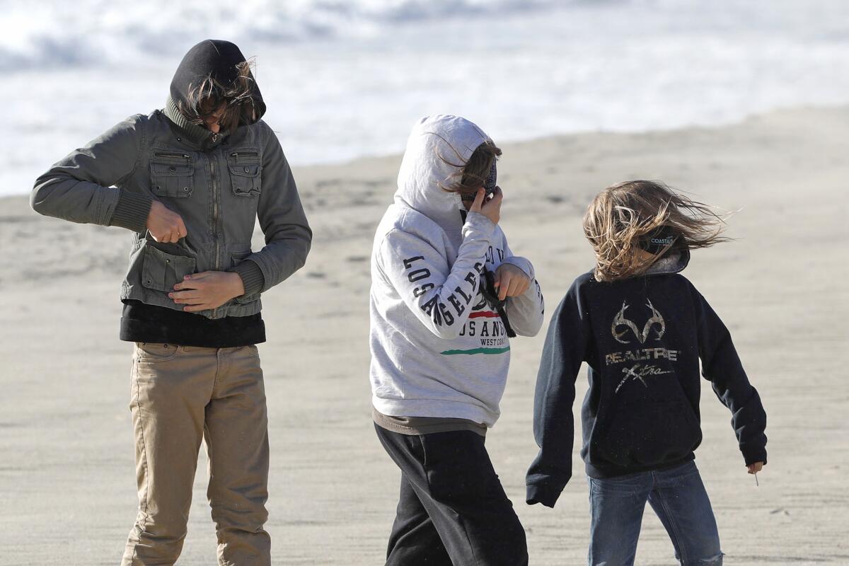 Three boys braves getting sand-blasted as they walk on Laguna's Main Beach on Monday.