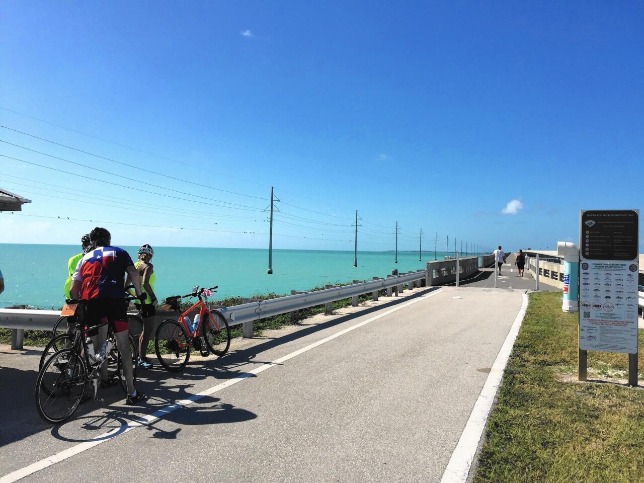 Cyclists take a break before heading onto Long Key Viaduct, one of the most scenic stretches of the ride. Cars travel on a bridge built parallel to the bike and pedestrian path.