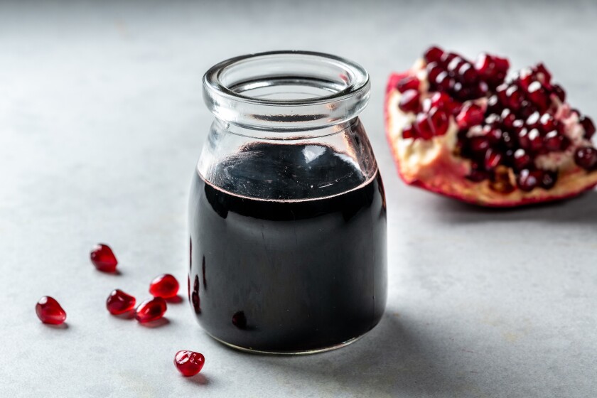 A jar of pomegranate molasses sits next to a piece of the fruit and loose arils.