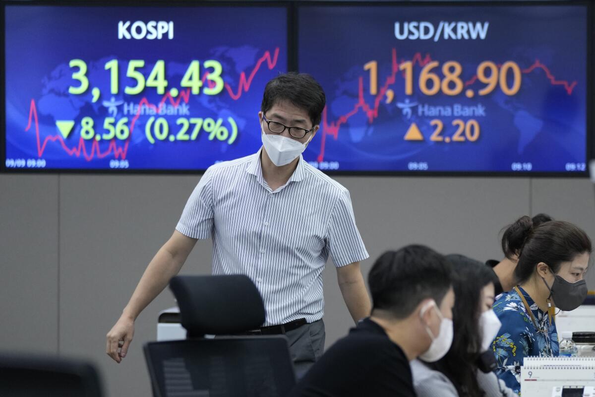 A currency trader passes by screens showing the Korea Composite Stock Price Index (KOSPI), left, and the foreign exchange rate between U.S. dollar and South Korean won at the foreign exchange dealing room of the KEB Hana Bank headquarters in Seoul, South Korea, Thursday, Sept. 9, 2021. Shares fell in Asia on Thursday after further losses on Wall Street following a Federal Reserve report showing U.S. economic activity slowed this summer. (AP Photo/Ahn Young-joon)