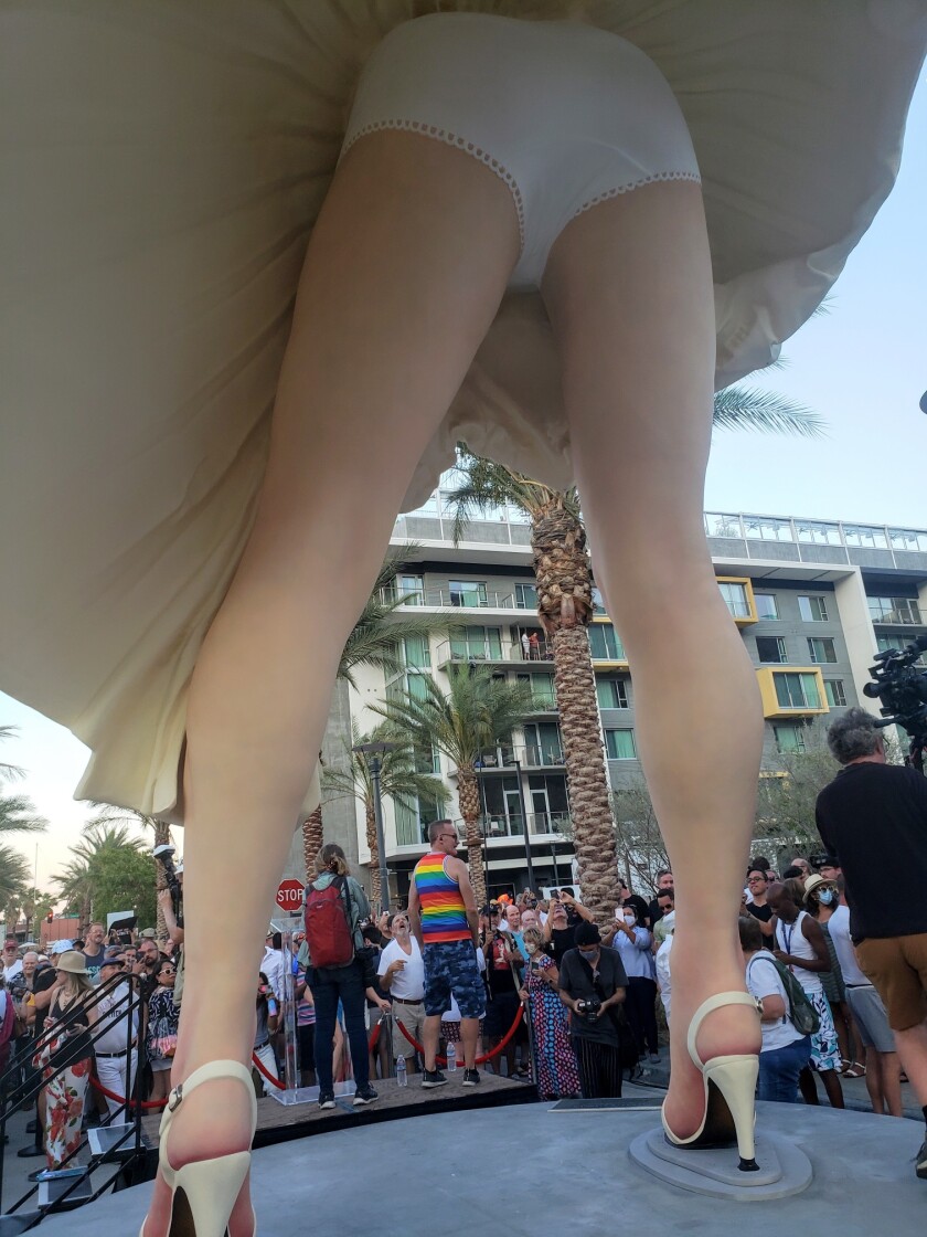 A man wearing a rainbow shirt is among those seen through the legs of a giant Marilyn Monroe statue with its skirt billowing