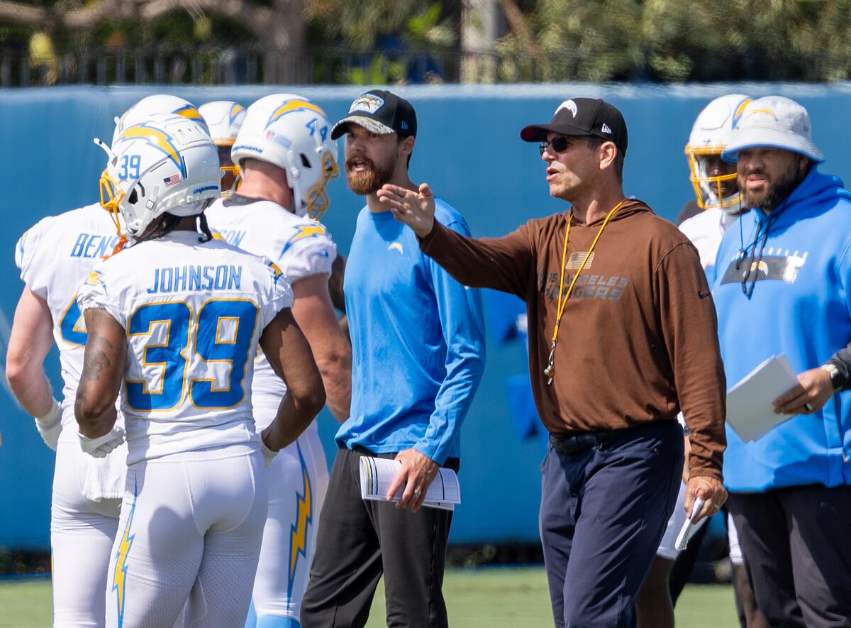 Coach Jim Harbaugh (brown hoodie) gestures to his Chargers on the practice field.