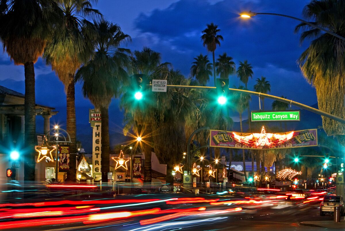 Cars move along a brightly lighted street lined with palm trees. 