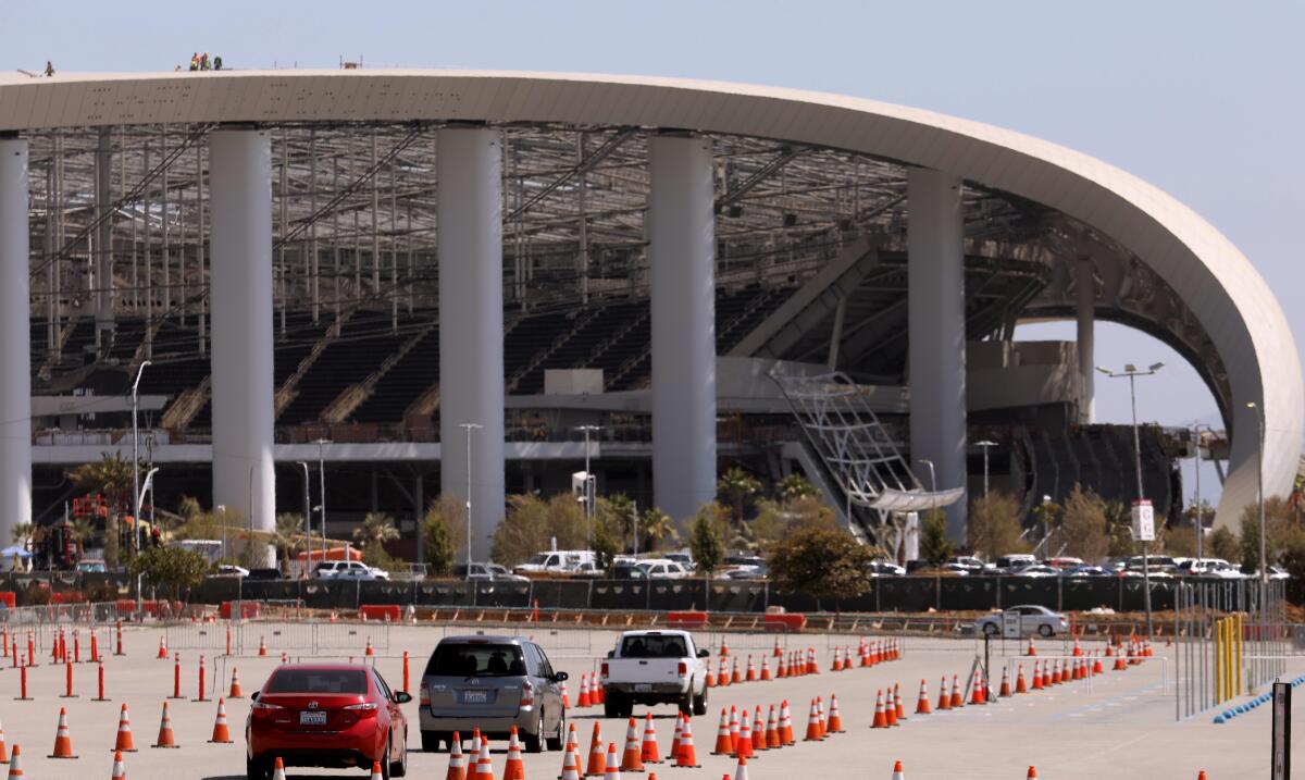 Cars exit the COVID-19 testing site at The Forum, with SoFi Stadium in the background.