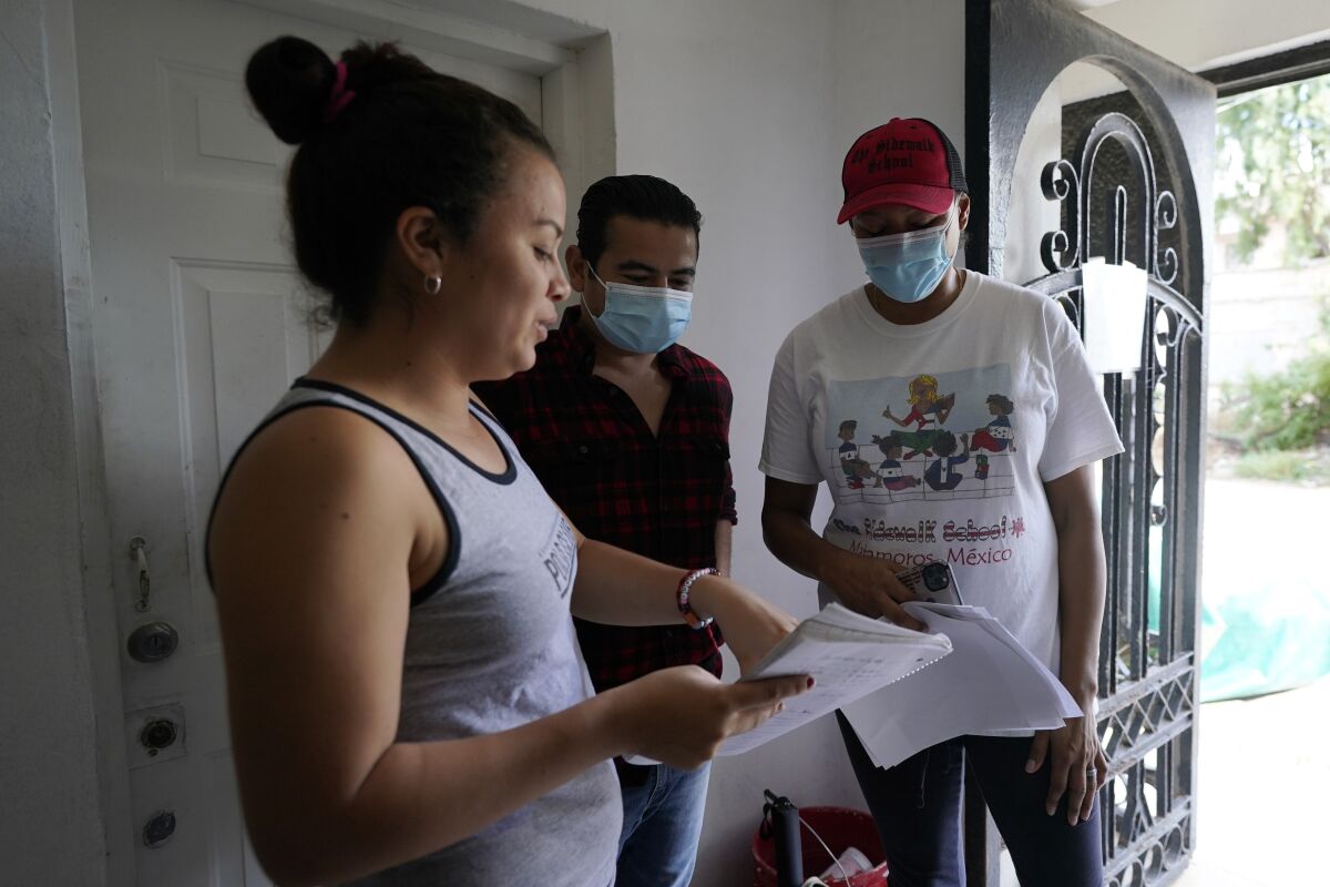 Sidewalk School founder Felicia Rangel-Samponaro, right, works with teacher Gabriela Fajardo, a 26-year-old Honduran seeking asylum in the United States, left, and assistant Victor Cavazos on Friday, Nov. 20, 2020, in Matamoros, Mexico. Like countless schools, the Sidewalk School went to virtual learning amid the coronavirus pandemic, but instead of being hampered by the change, it has blossomed. (AP Photo/Eric Gay)