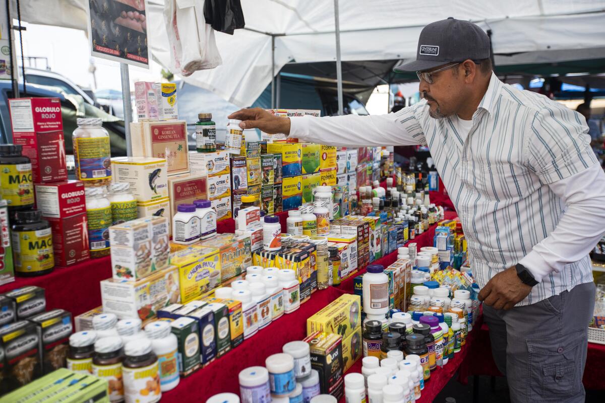 A man organizes a table of vitamins and supplements at an outdoor swap meet