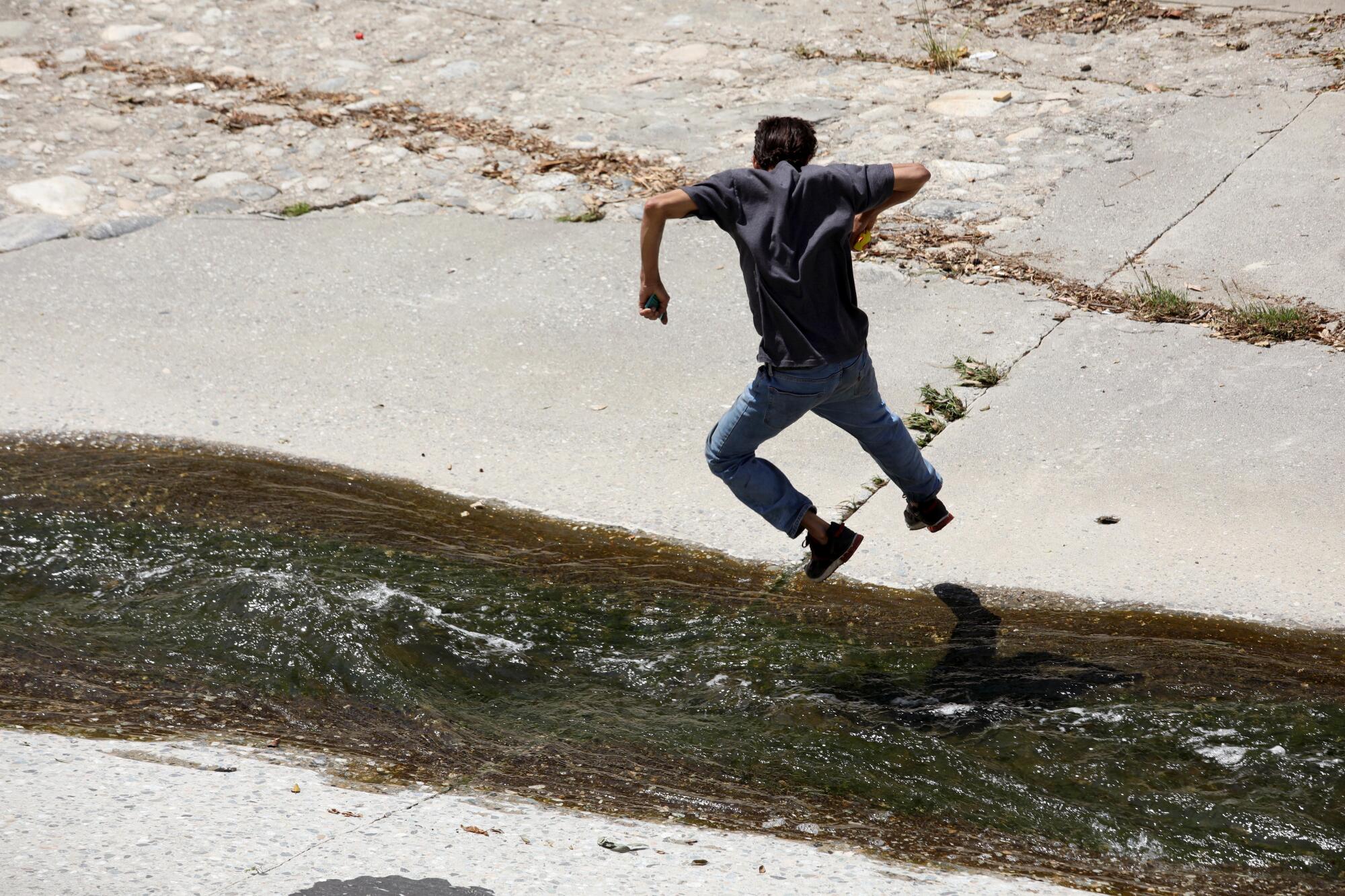 Cesar Augusto jumps across the Arroyo Seco to get to his makeshift home along the 110 Freeway in Los Angeles.