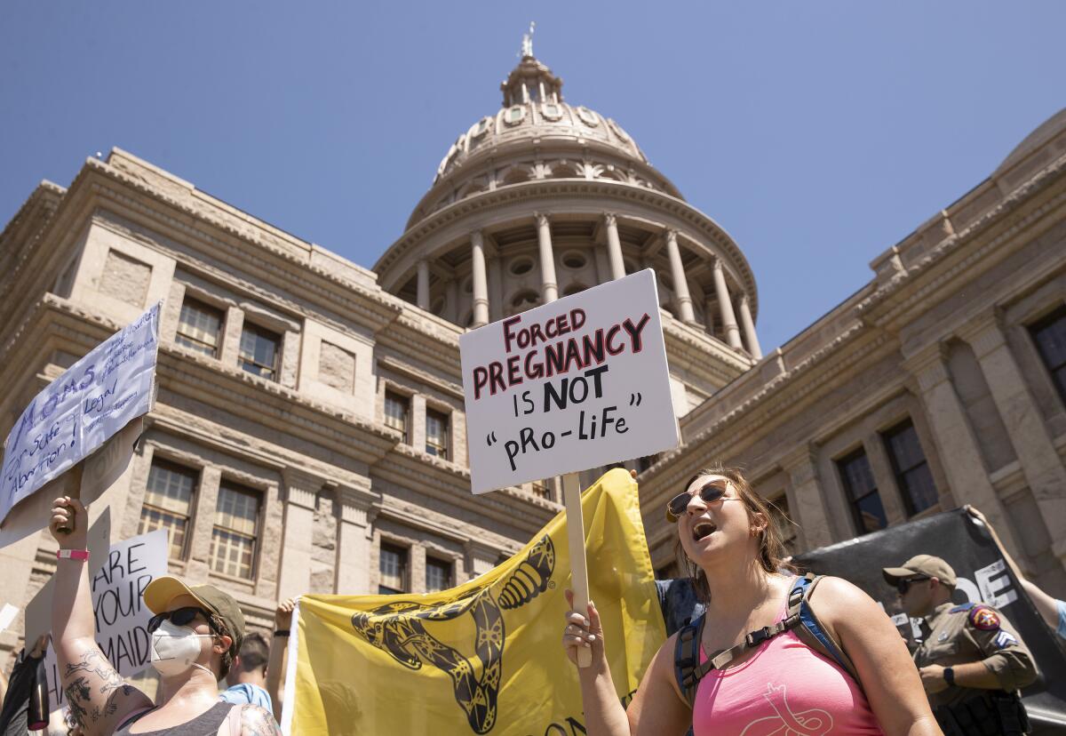 People hold protest signs, one reading "Forced pregnancy is not 'pro-life'" in front of the Texas Capitol in Austin.