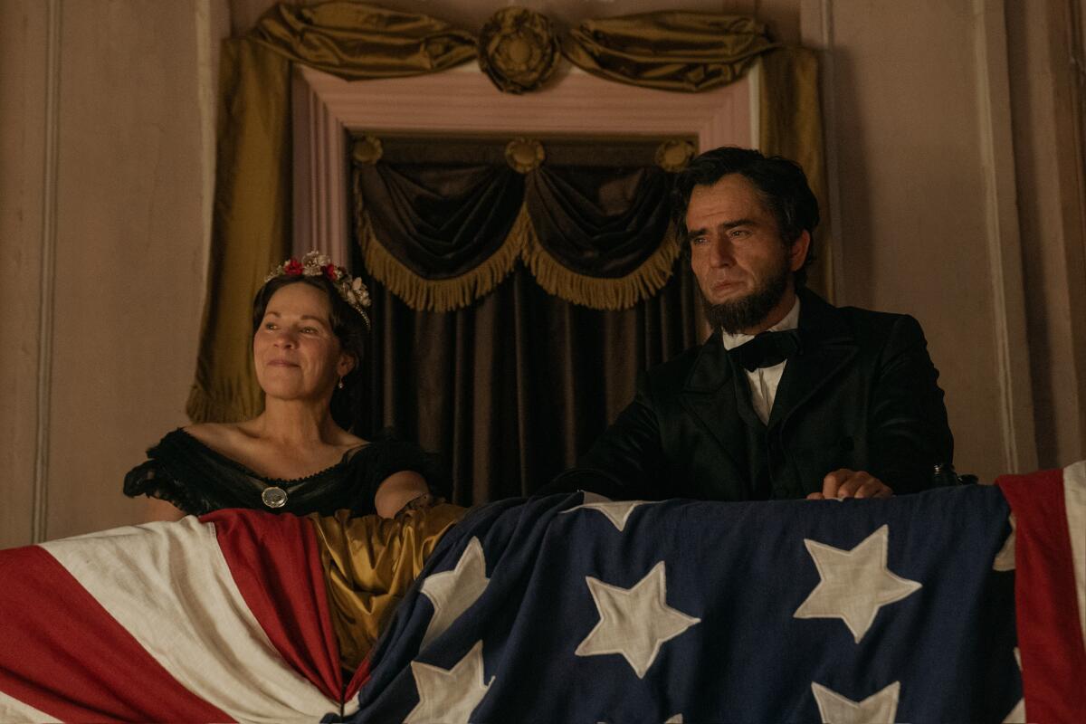 A woman and a man sit in a theater booth with an American  flag draped over the railing.